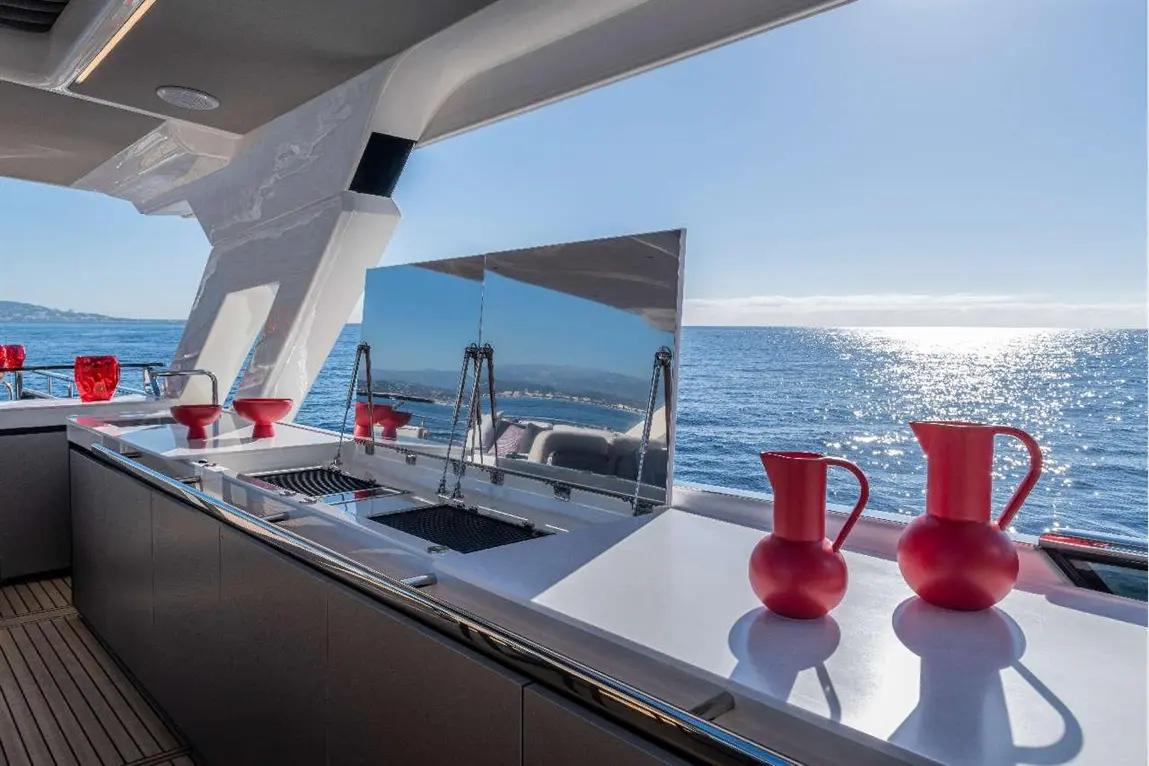 A modern yacht kitchen features two red pitchers on a white countertop, overlooking the ocean under a clear blue sky.